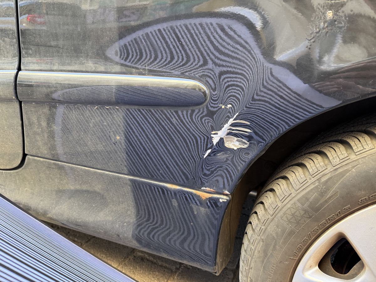 Prüfkarte des Sachverständigen, deren Streifenmuster sich im Lack eines Peugeot 206 CC spiegelt und die Verformung sichtbar macht